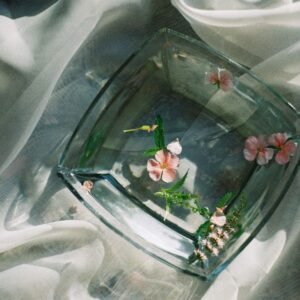 Aesthetic top view of floating flowers in a glass bowl on soft fabric, providing a serene and elegant composition.